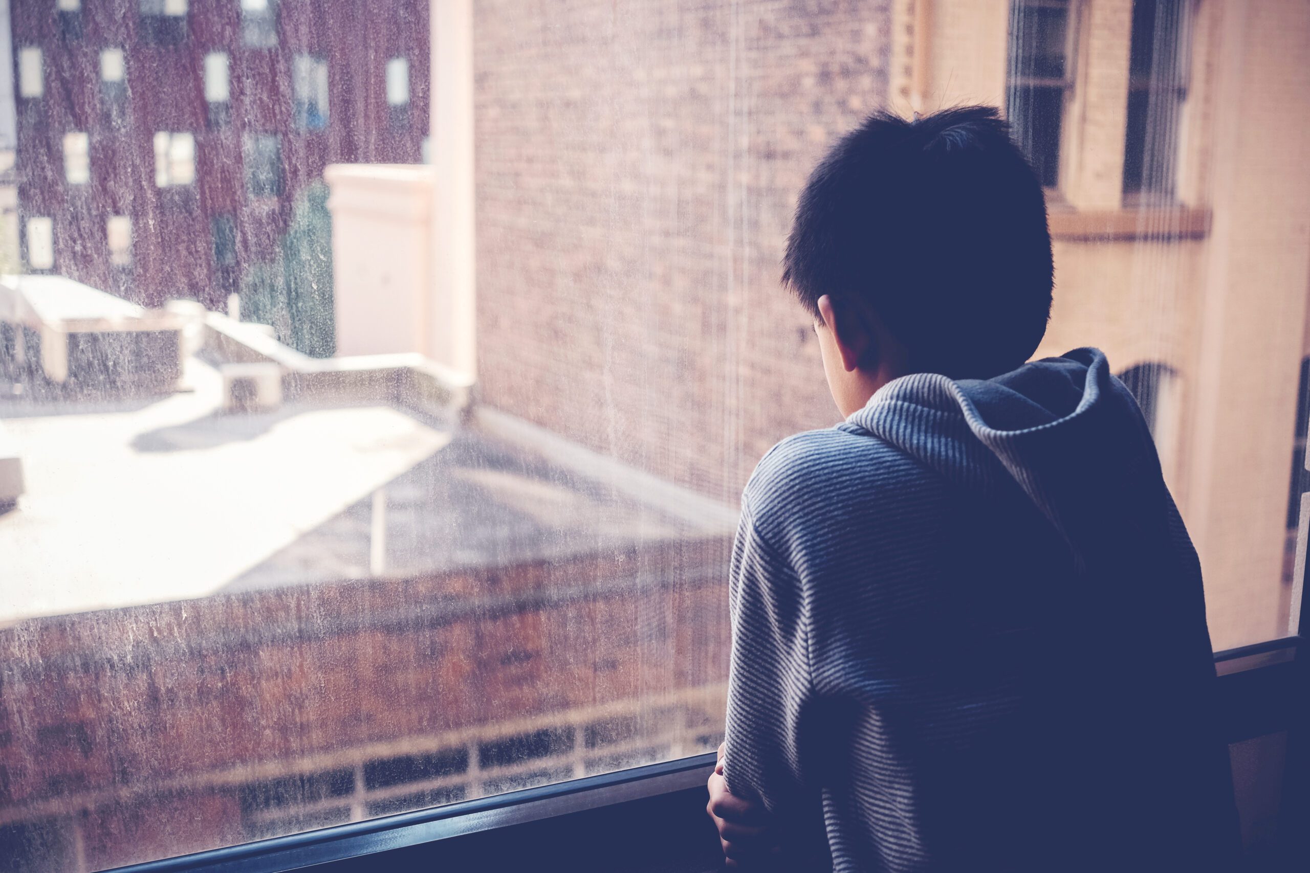 Sad Asian preteen boy feeling lonely, looking out of window from Studie 2022: Cybermobbing in Pandemiezeiten